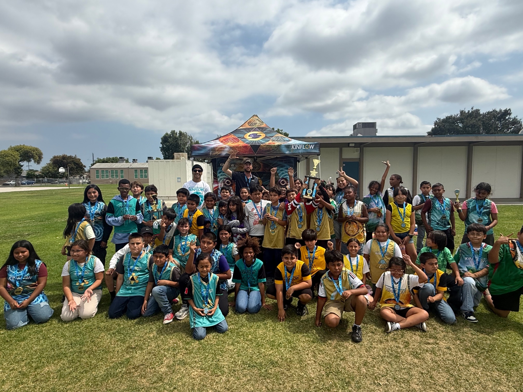 KinFlow players celebrating with medals and trophies in front of the KinFlow tent at a school tournament